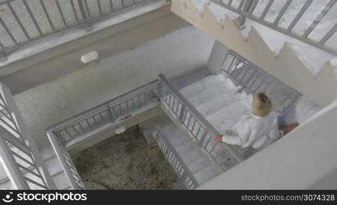 High-angle shot of a couple walking down the spiral stairs in multi-storey house holding hands.