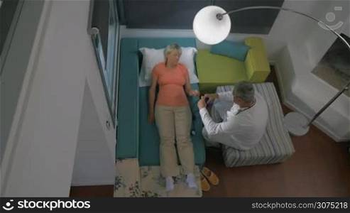 High angle shot of a doctor visiting sick senior woman at home and checking her blood pressure
