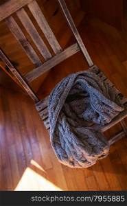 High angle shot of a woollen scarf lying on simple wooden chair. Sunlight on the floor. Woollen scarf lying on wooden chair