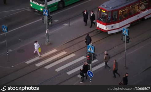 High angle shot of people crossing the road on green traffic light in the evening. Bus and tram waiting