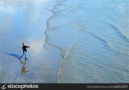 High angle side view of mature man on beach throwing stones into ocean