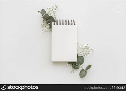 high angle view empty spiral notepad with leafs baby s breath flowers white surface