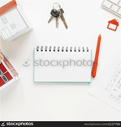 high angle view house model near spiral notepad with keys pen white background