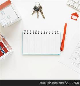 high angle view house model near spiral notepad with keys pen white background