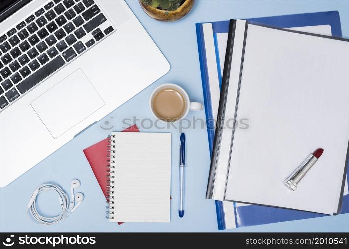 high angle view laptop folders coffee cup earphone spiral notepad pen against blue background