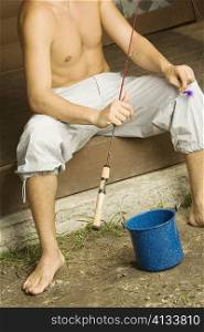 High angle view of a bare chested young man sitting on the porch holding a fishing rod