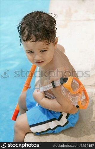 High angle view of a boy holding snorkel sitting by the pool