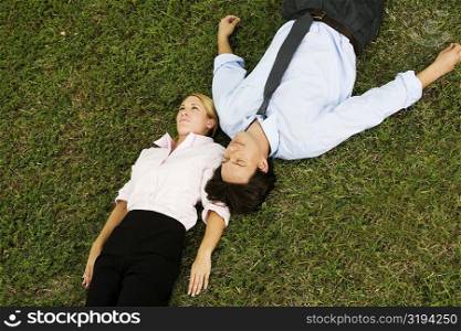 High angle view of a businessman and a businesswoman lying on the grass