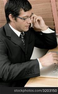 High angle view of a businessman sitting in front of a laptop using a mobile phone