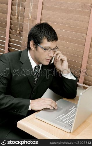 High angle view of a businessman sitting in front of a laptop using a laptop and talking on a mobile phone