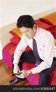 High angle view of a businessman sitting on the bed and operating a mobile phone