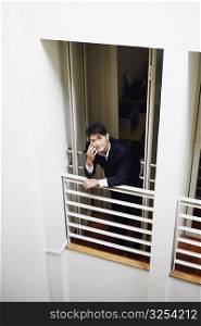 High angle view of a businessman standing at the doorway in an office and talking on a mobile phone