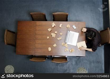 High angle view of a businessman writing on a notepad with crushed papers on the table