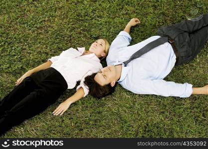 High angle view of a businesswoman and a businessman lying on the grass