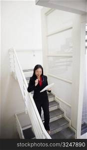 High angle view of a businesswoman holding a newspaper and walking down a staircase