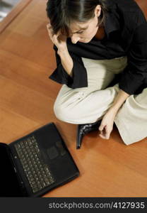 High angle view of a businesswoman talking on a mobile phone and sitting in front of a laptop