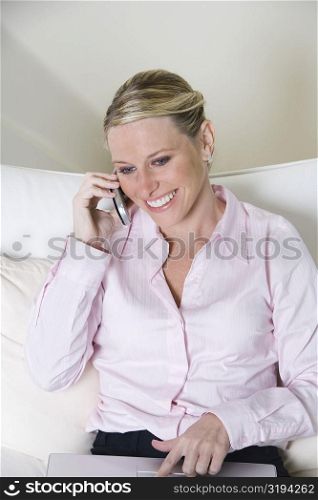 High angle view of a businesswoman talking on a mobile phone while working on a laptop