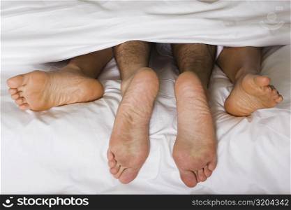 High angle view of a couple&acute;s feet under the sheets of a bed