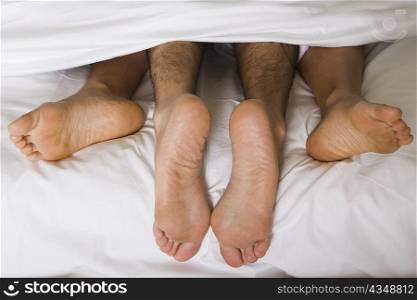 High angle view of a couple&acute;s feet under the sheets of a bed