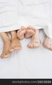 High angle view of a couple&acute;s feet with their child on the bed