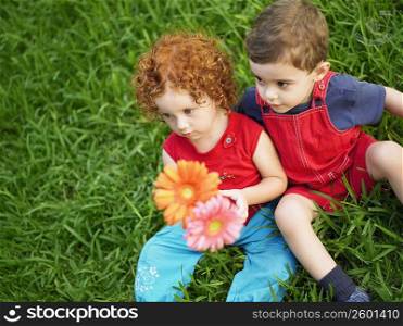 High angle view of a girl and her brother holding artificial flowers