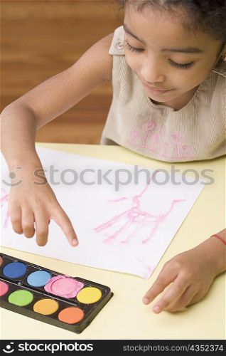 High angle view of a girl making handprint on a sheet of paper
