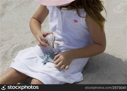 High angle view of a girl playing with a conch shell and a starfish on the beach