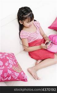 High angle view of a girl sitting on a couch and listening to an MP3 player