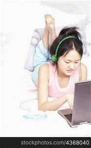 High angle view of a girl using a laptop listening to music on an MP3 player