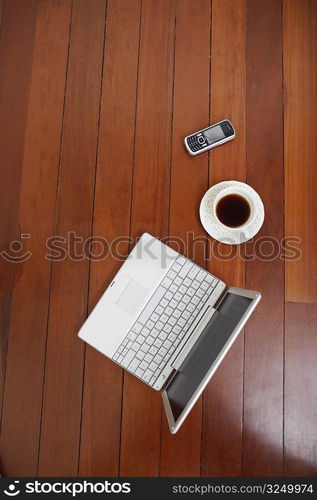 High angle view of a laptop and a mobile phone with a tea cup on a hardwood floor