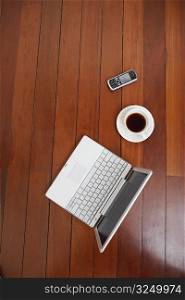 High angle view of a laptop and a mobile phone with a tea cup on a hardwood floor