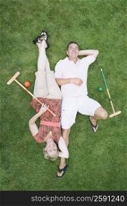High angle view of a mature couple lying on grass with bocce balls and sticks