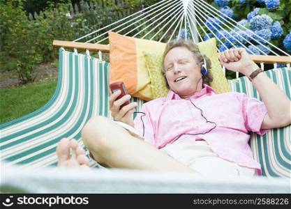 High angle view of a mature man listening to music and lying in a hammock