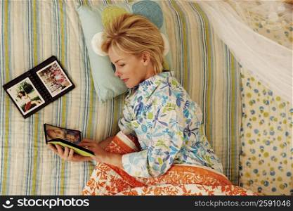 High angle view of a mature woman lying in bed and looking at a photo album