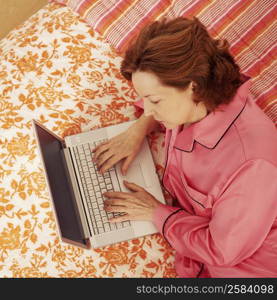 High angle view of a mature woman lying in bed using a laptop