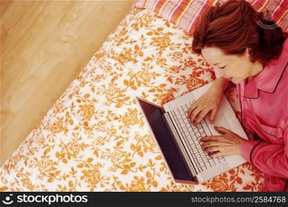 High angle view of a mature woman lying in bed using a laptop