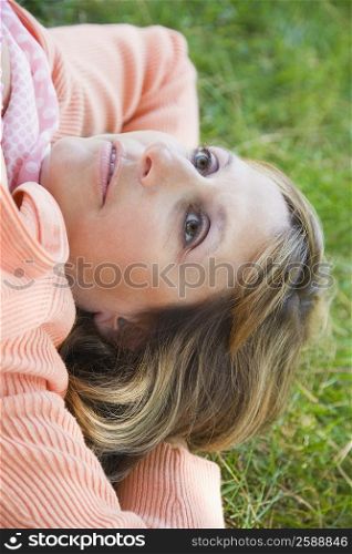 High angle view of a mature woman lying on grass with her hands behind her head
