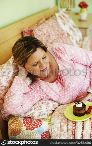 High angle view of a mature woman lying on the bed and holding a plate of cake