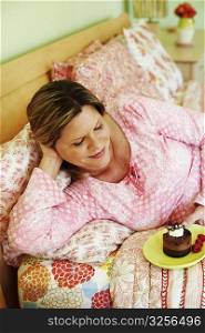 High angle view of a mature woman lying on the bed and holding a plate of cake
