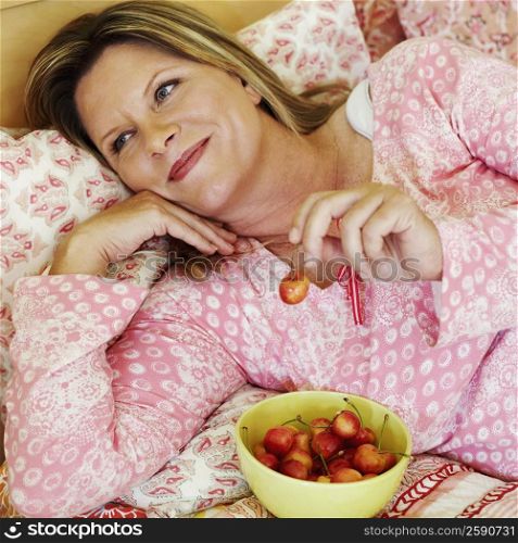 High angle view of a mature woman lying on the bed with a bowl of cherries