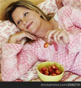 High angle view of a mature woman lying on the bed with a bowl of cherries