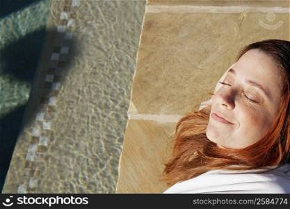 High angle view of a mature woman lying with her eyes closed at the poolside