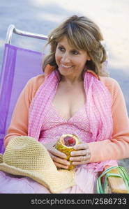 High angle view of a mature woman reclining on a deck chair and holding a pineapple