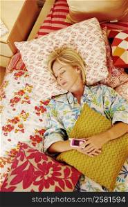 High angle view of a mature woman sleeping on the bed holding a mobile phone