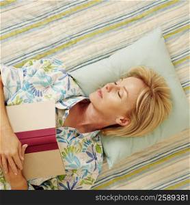 High angle view of a mature woman sleeping on the bed with a book