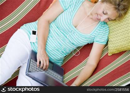 High angle view of a mature woman using a laptop while listening to music in a hammock