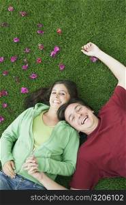 High angle view of a mid adult man and a young woman lying on the grass and laughing