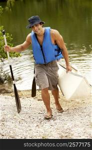 High angle view of a mid adult man carrying a kayak and an oar