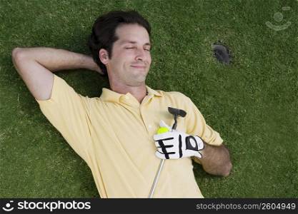 High angle view of a mid adult man lying on a golf course with a golf ball and a golf club
