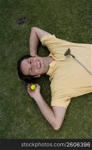High angle view of a mid adult man lying on a golf course and holding a golf ball